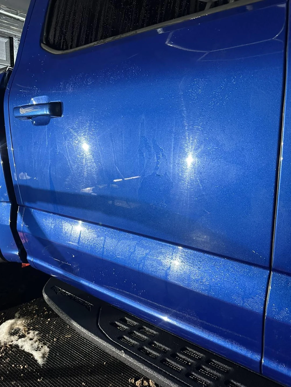 Puertas del vehículo azul con marcas circulares visibles bajo la luz de inspección